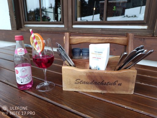 Staudachstub’n Ein Holzkasten mit Besteck, einer Getränkeflasche und einem Cocktail mit Zitrusfrucht.