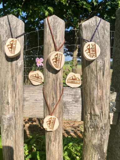 Durchnermühle Holzscheiben mit verschiedenen Gravuren hängen an Pfosten, umgeben von Natur.