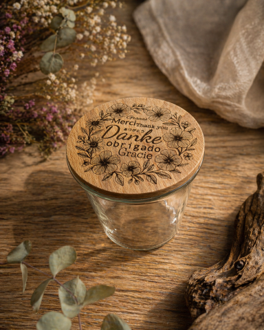 Ein Glasbehälter mit Holzdeckel und floralem Design auf einem Holztisch.