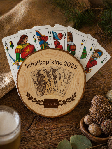 Spielkarten mit Holzbrett für Schafkopfwettbewerb 2025, umgeben von Bier und Eicheln.