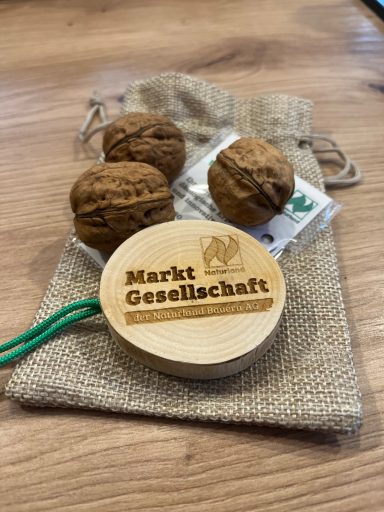 Naturland Marktgesellschaft Drei Nüsse und ein Holzbrett mit der Aufschrift "Markt Gesellschaft" auf einem Leinenbeutel.