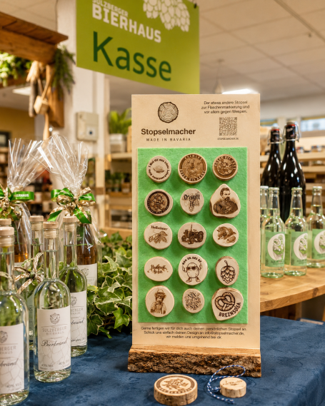 Verkaufsdisplay "original Stopsel" Holzständer mit verschiedenen Medaillen und Flaschen im Hintergrund. Kasse sichtbar.