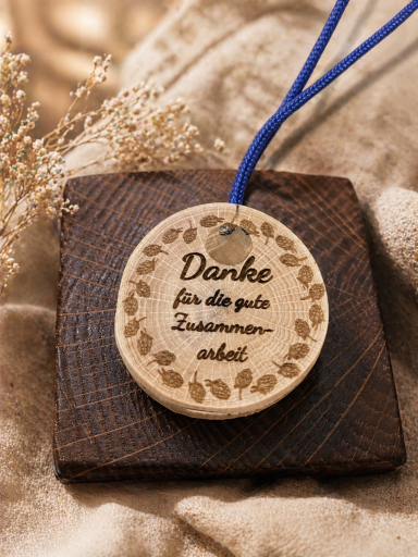 Holzscheibe mit der Aufschrift "Danke für die gute Zusammenarbeit" auf einem braunen Untergrund.